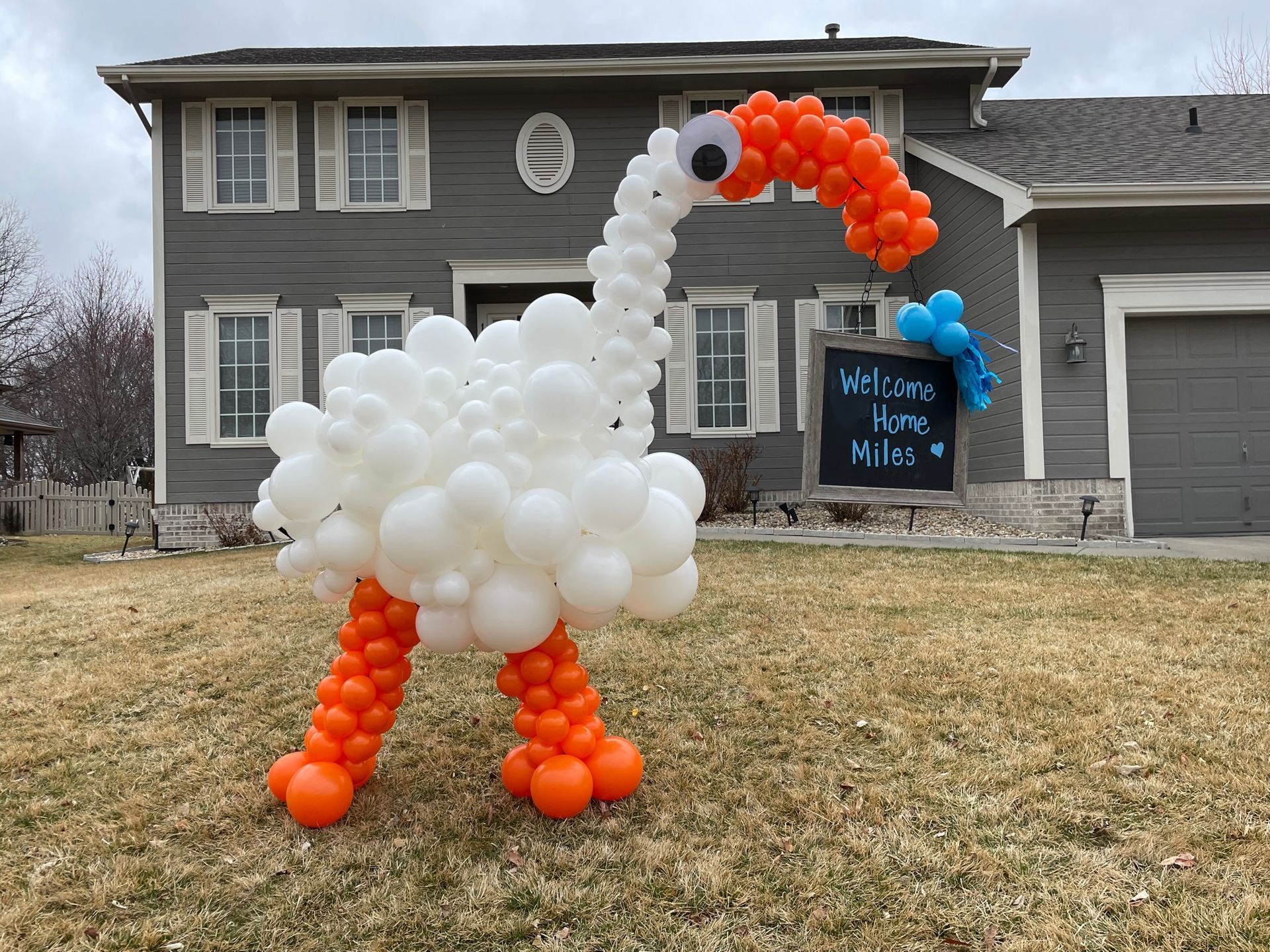 A swan made out of balloons in front of a house.