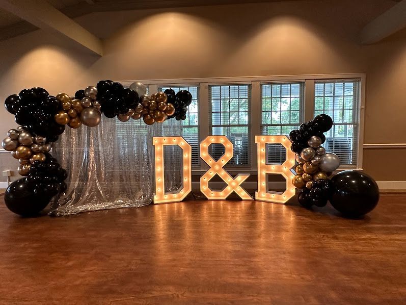 A room decorated with black and gold balloons and lighted letters.