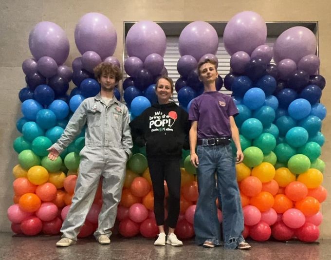 A woman in a dress is holding balloons and smiling.