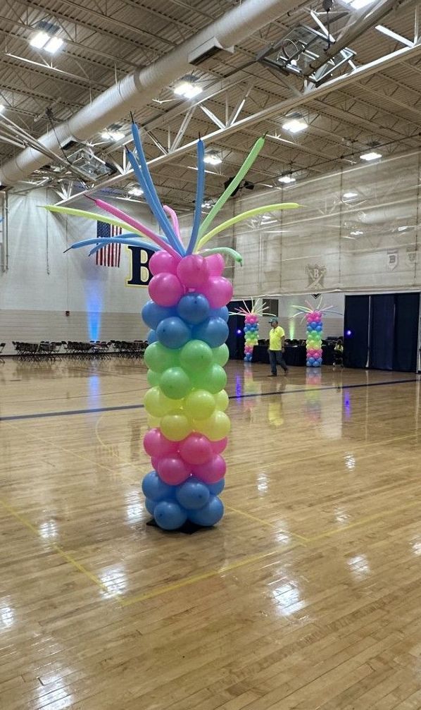 A balloon pillar is sitting on top of a wooden floor in a gym.