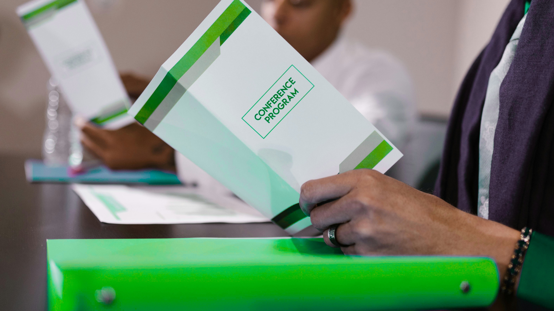 A woman is holding a green binder and looking at a brochure.