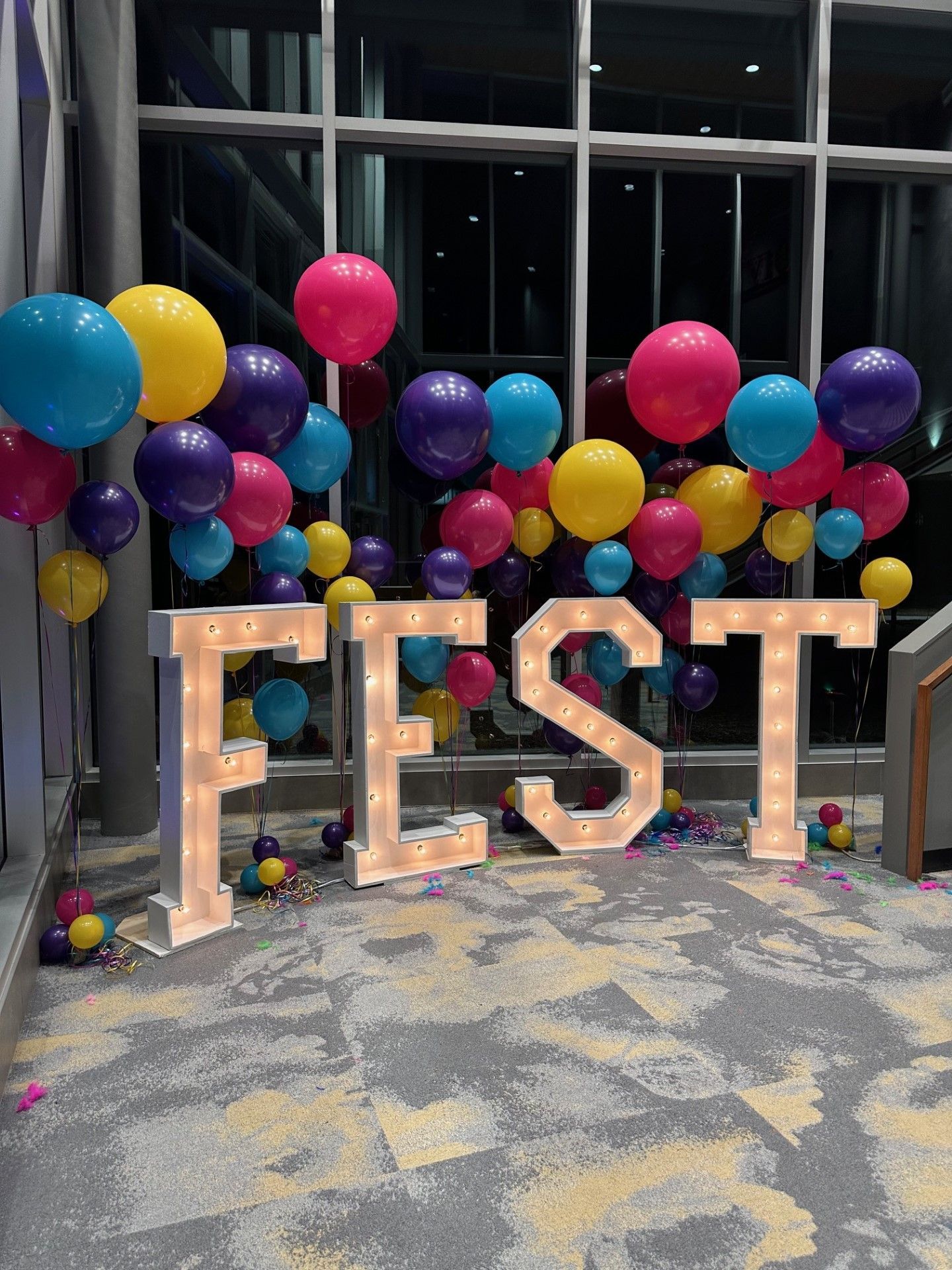 The word fest is surrounded by colorful balloons and lights.