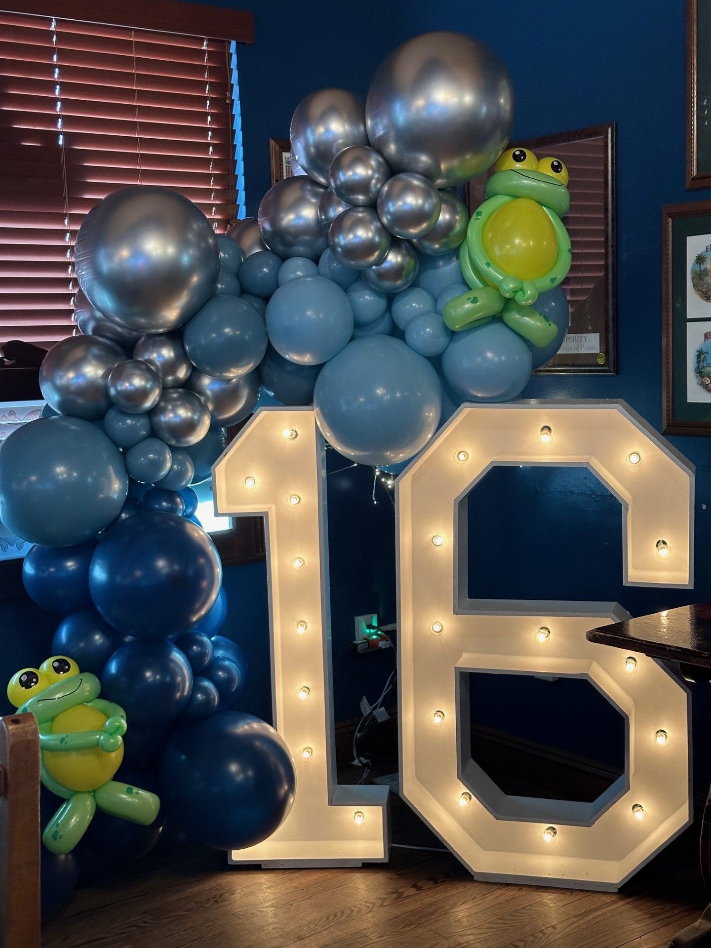 A large number 16 is surrounded by balloons and frogs.