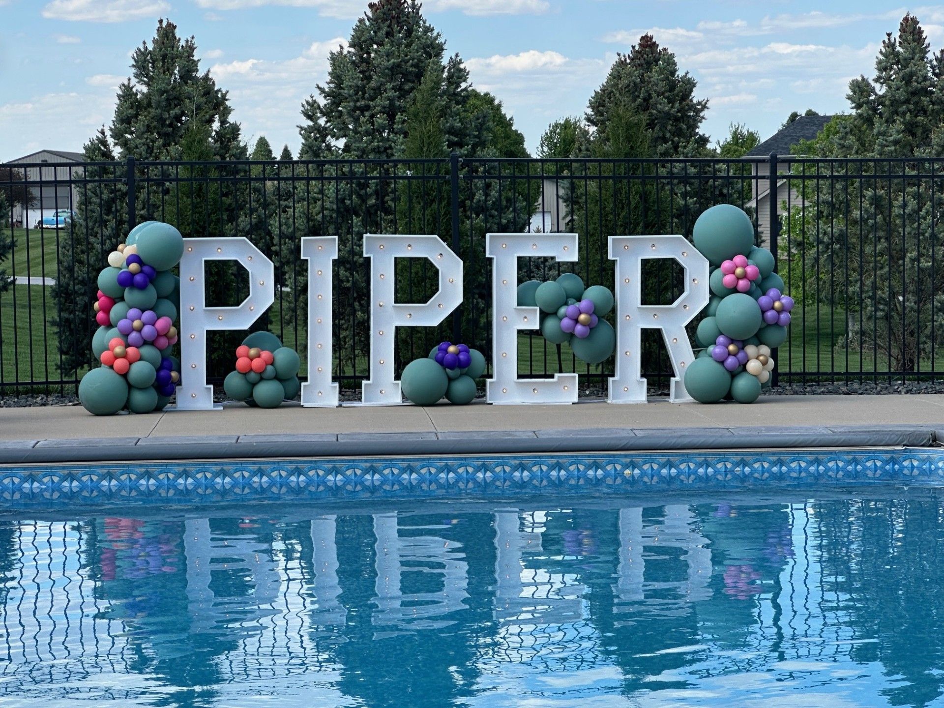 The word piper is surrounded by balloons next to a pool.