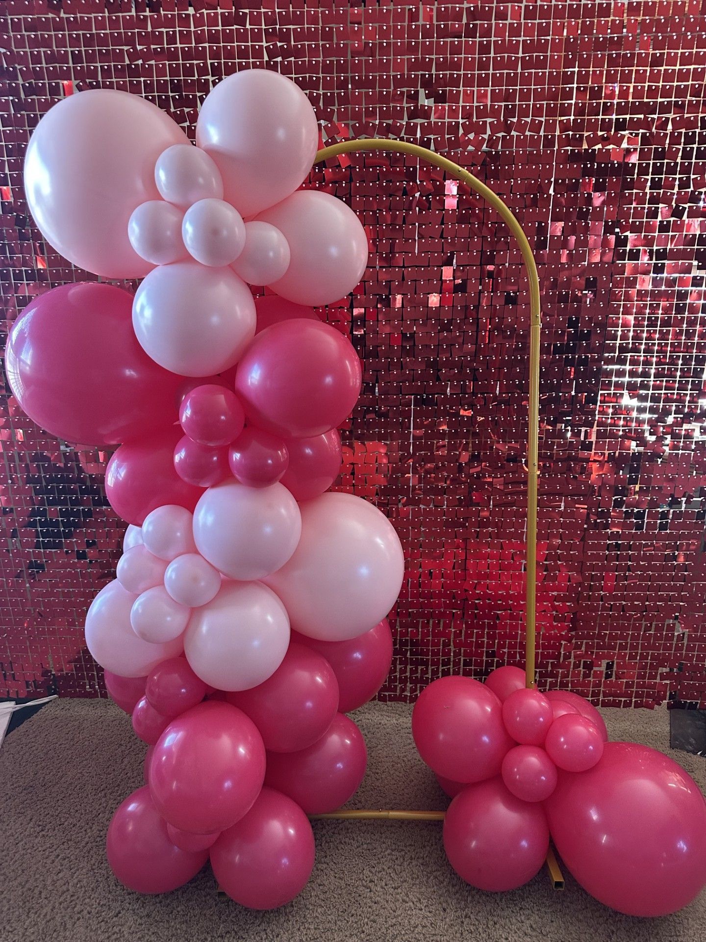 A bunch of pink and white balloons are sitting on the floor in front of a red wall.
