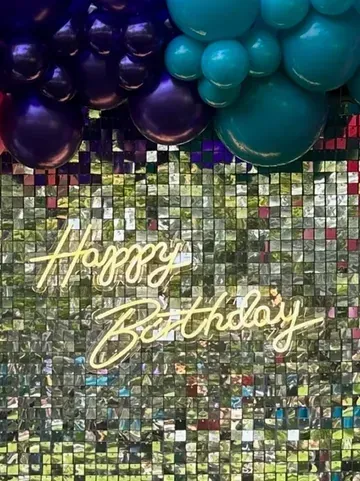 A neon sign that says `` happy birthday '' is hanging on a wall with balloons.