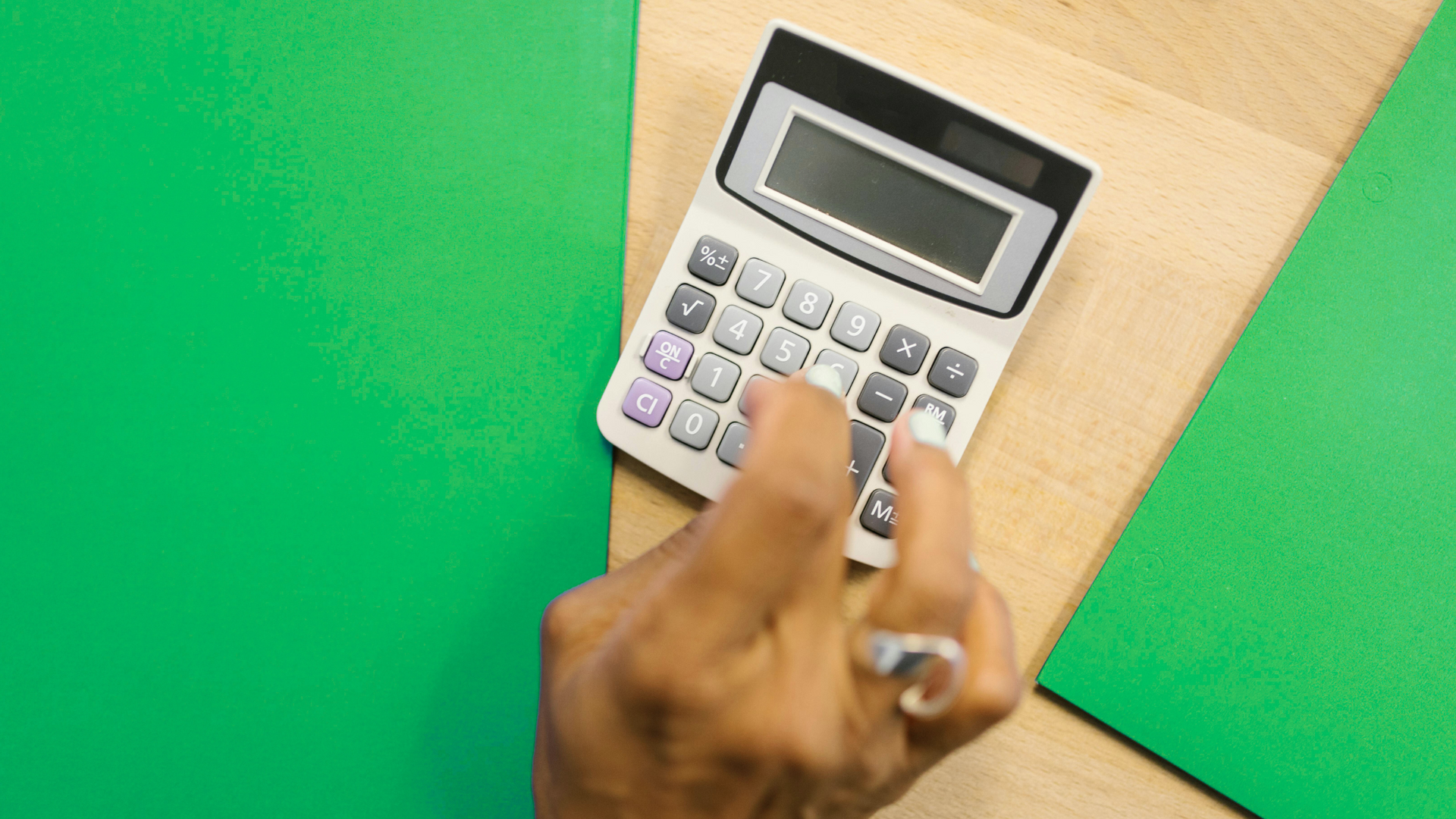 A person is using a calculator on a green table.