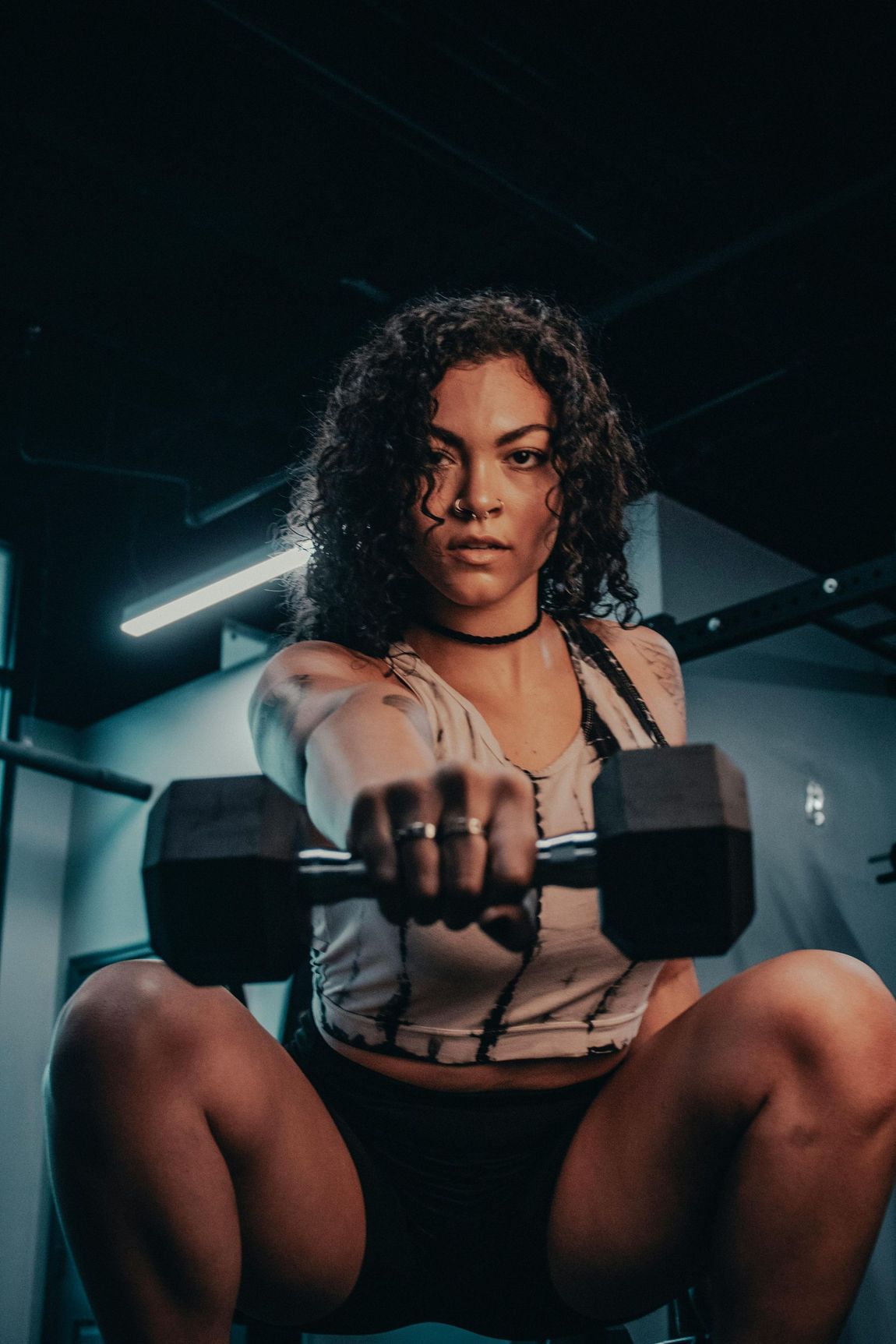 A woman is squatting down while holding a dumbbell in a gym.