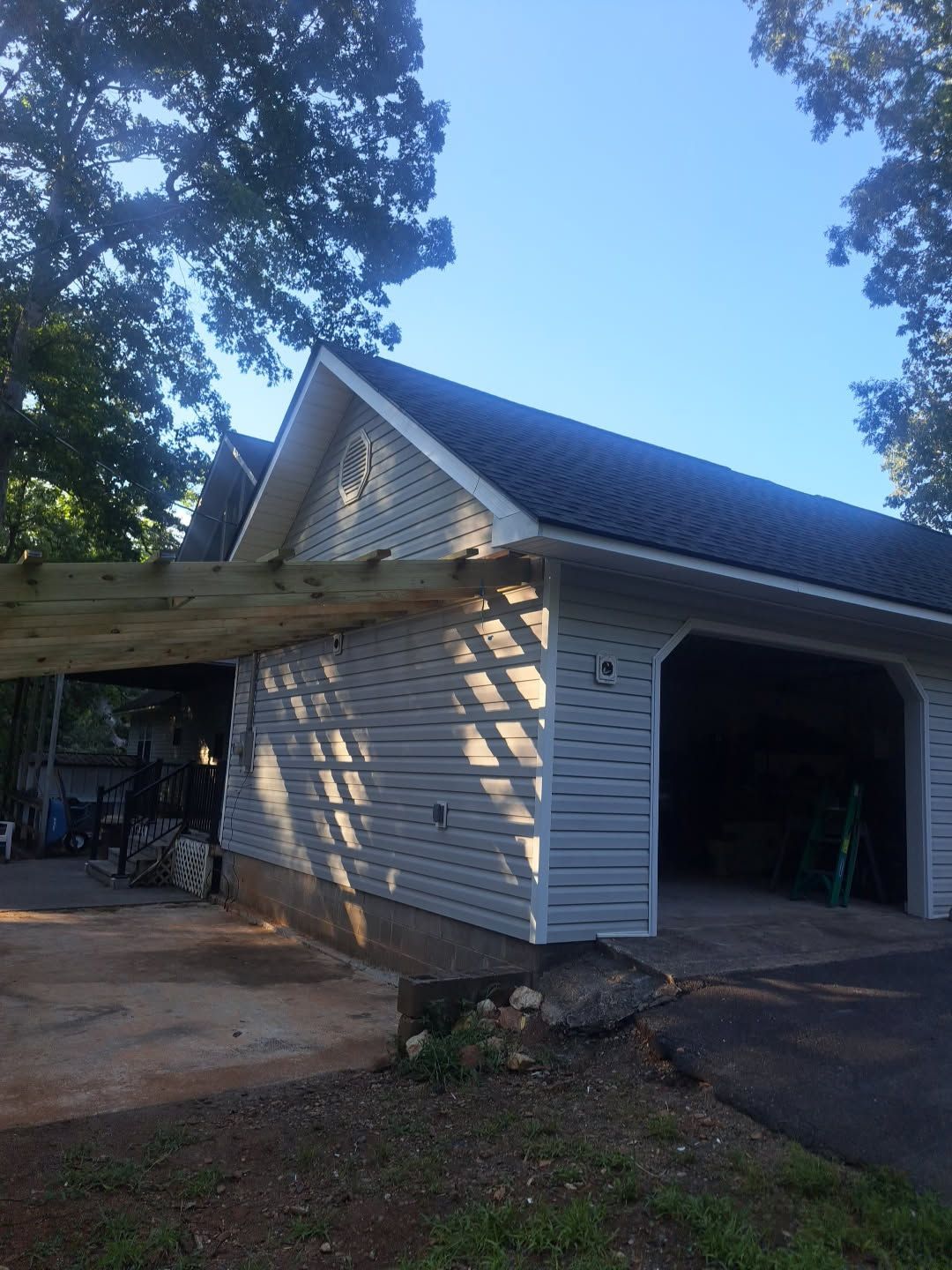 White detached garage with open bay, driveway, and trees in bright daylight.
