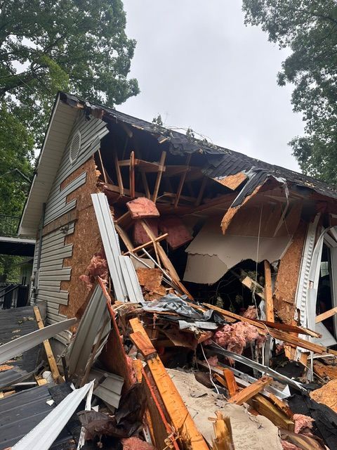 Severely damaged house with collapsed roof, broken siding, and debris after a structural collapse.