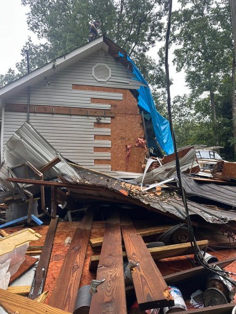 Collapsed house wall with debris piled in front and blue tarp covering part of the roof.