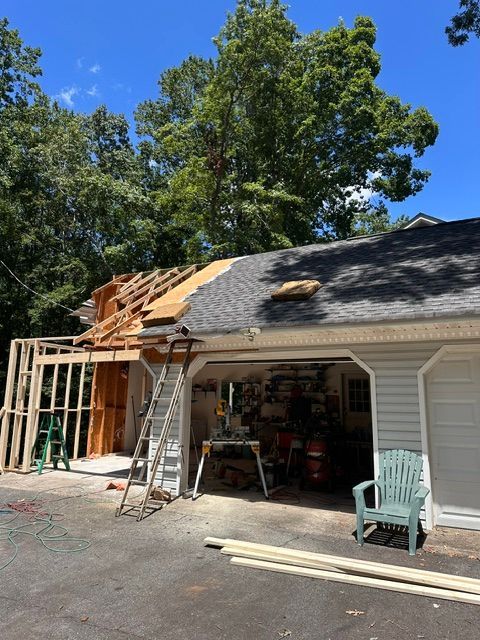 Garage under construction with exposed roof framing, ladder, and tools beside a white house.