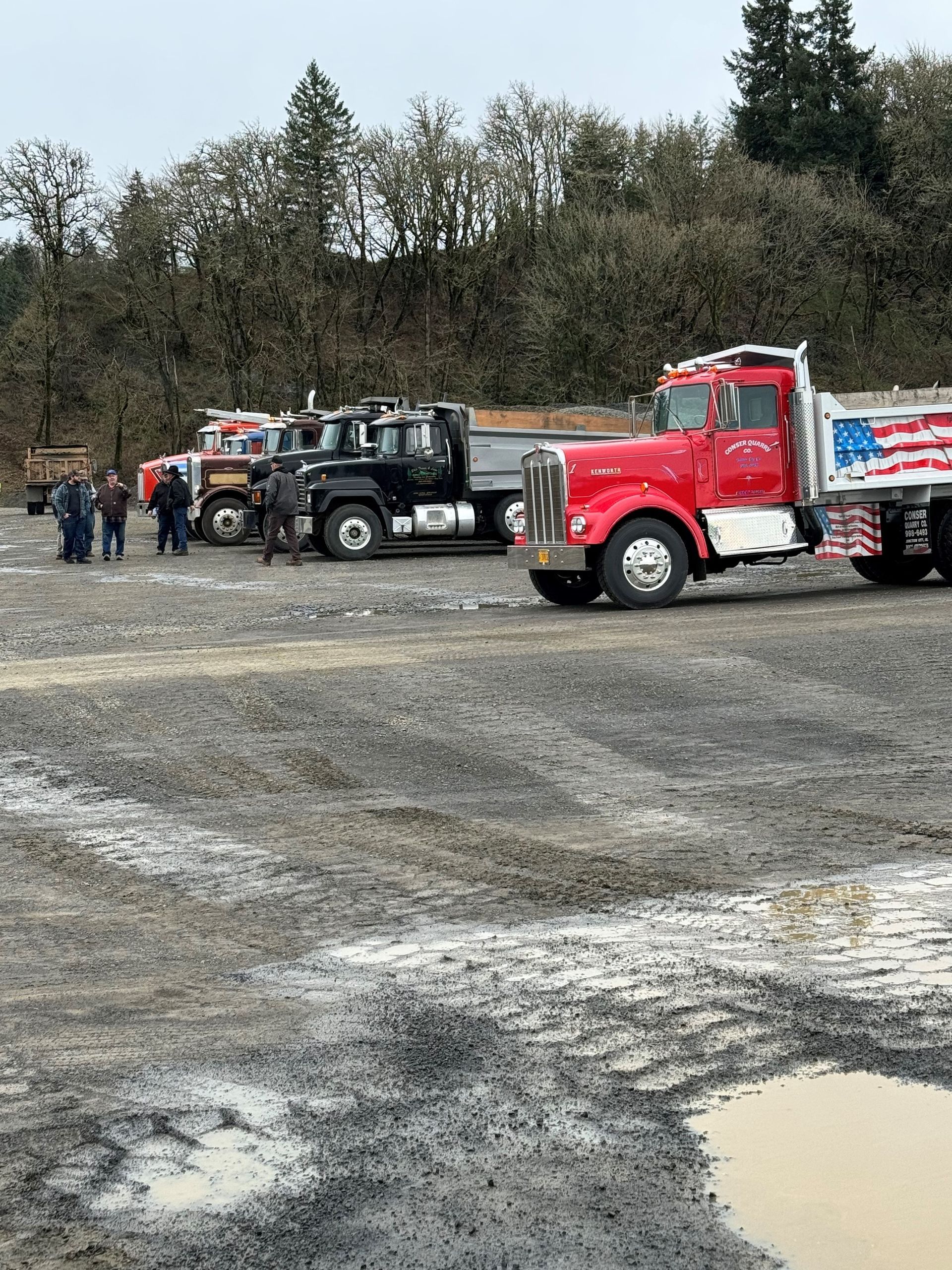 A row of trucks are parked in a muddy field.