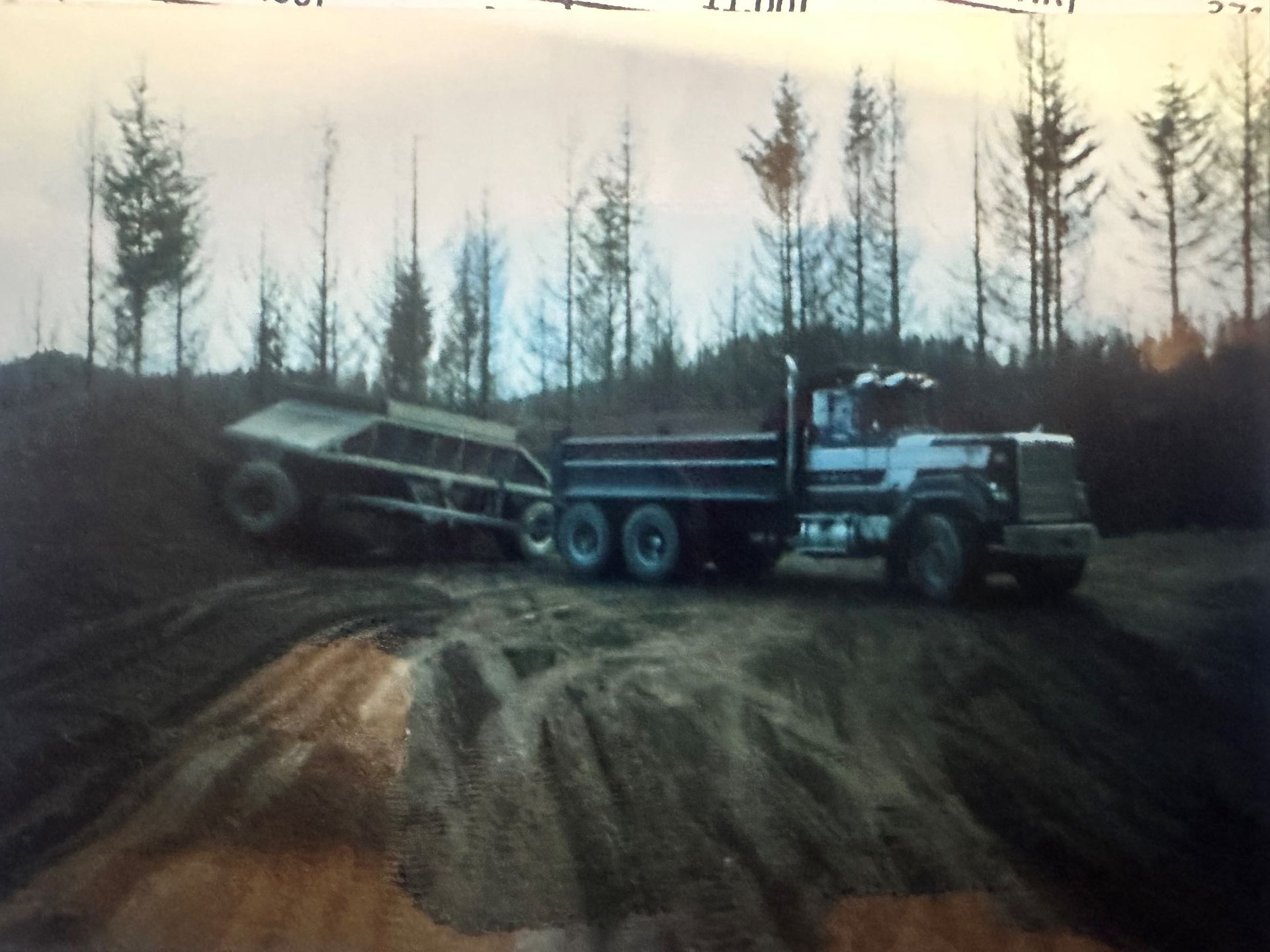 A dump truck is driving down a dirt road with trees in the background