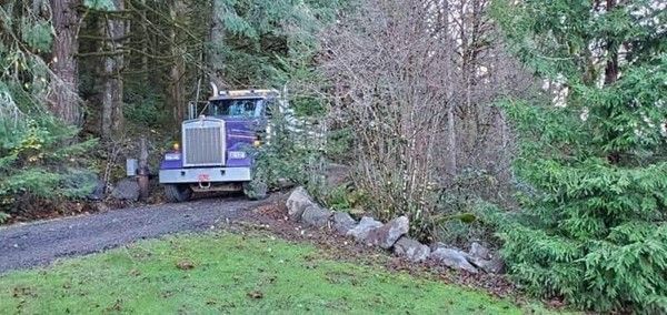 A purple semi truck is driving down a dirt road.
