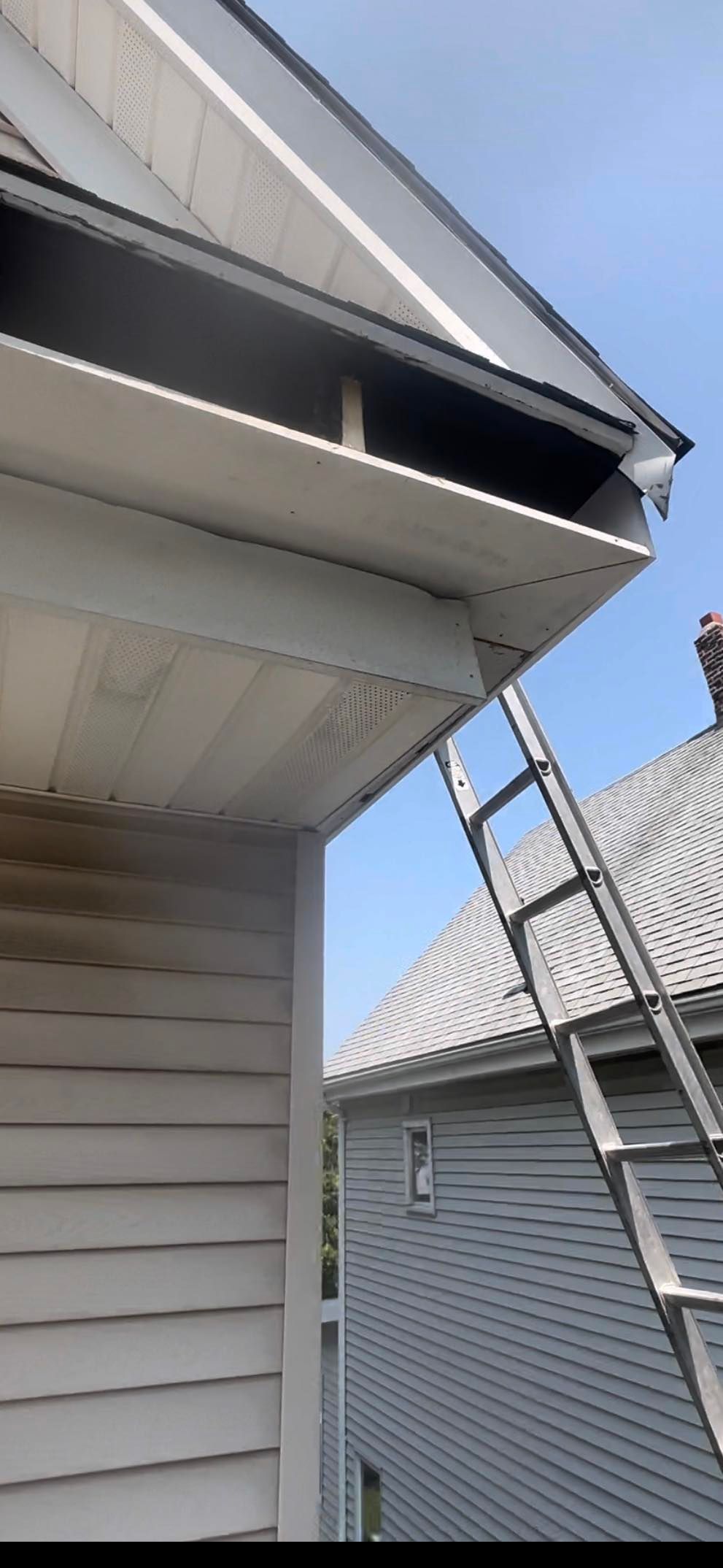A man is standing on the roof of a house with a ladder attached to it.