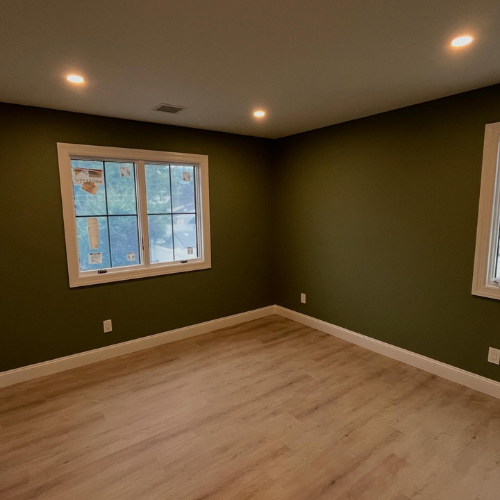 An empty room with green walls and wooden floors and two windows.