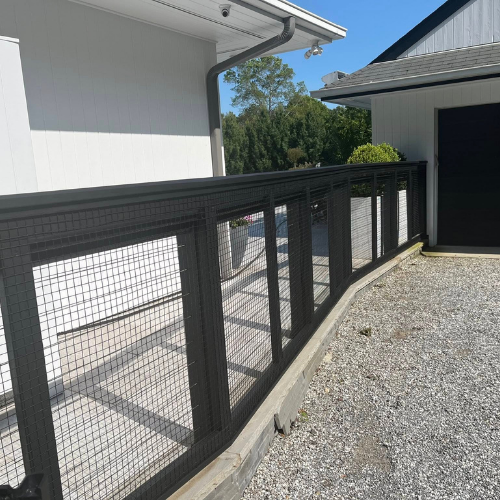 A black fence surrounds a gravel driveway in front of a white house