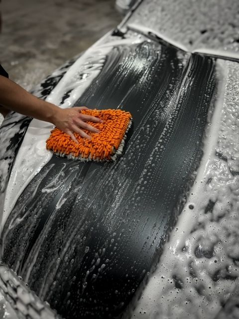 A person is washing a car with a sponge and foam.