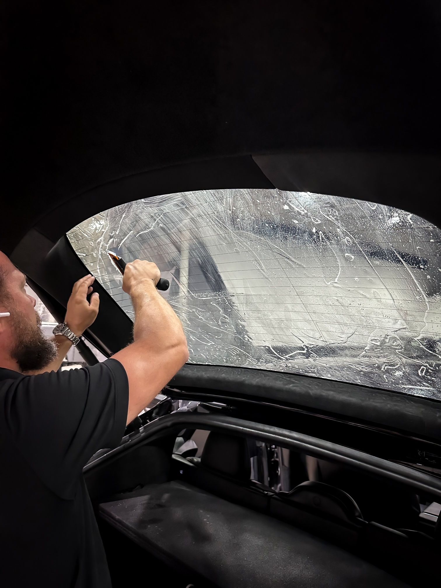 A man is cleaning the windshield of a car with a brush.