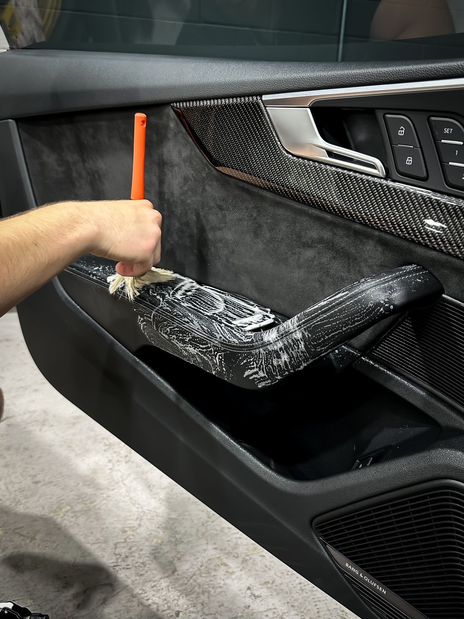 A person is cleaning the door panel of a car with a brush.