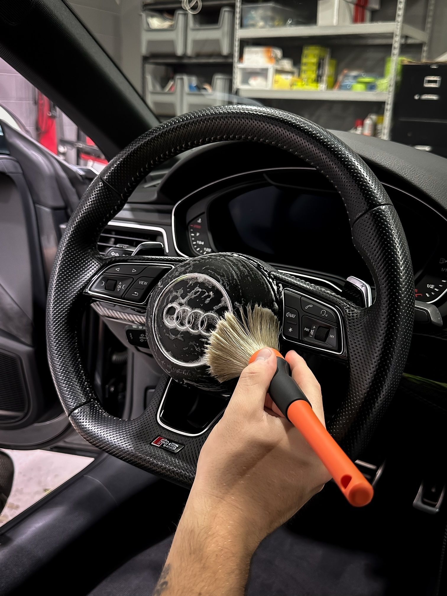 A person is cleaning the steering wheel of a car with a brush.