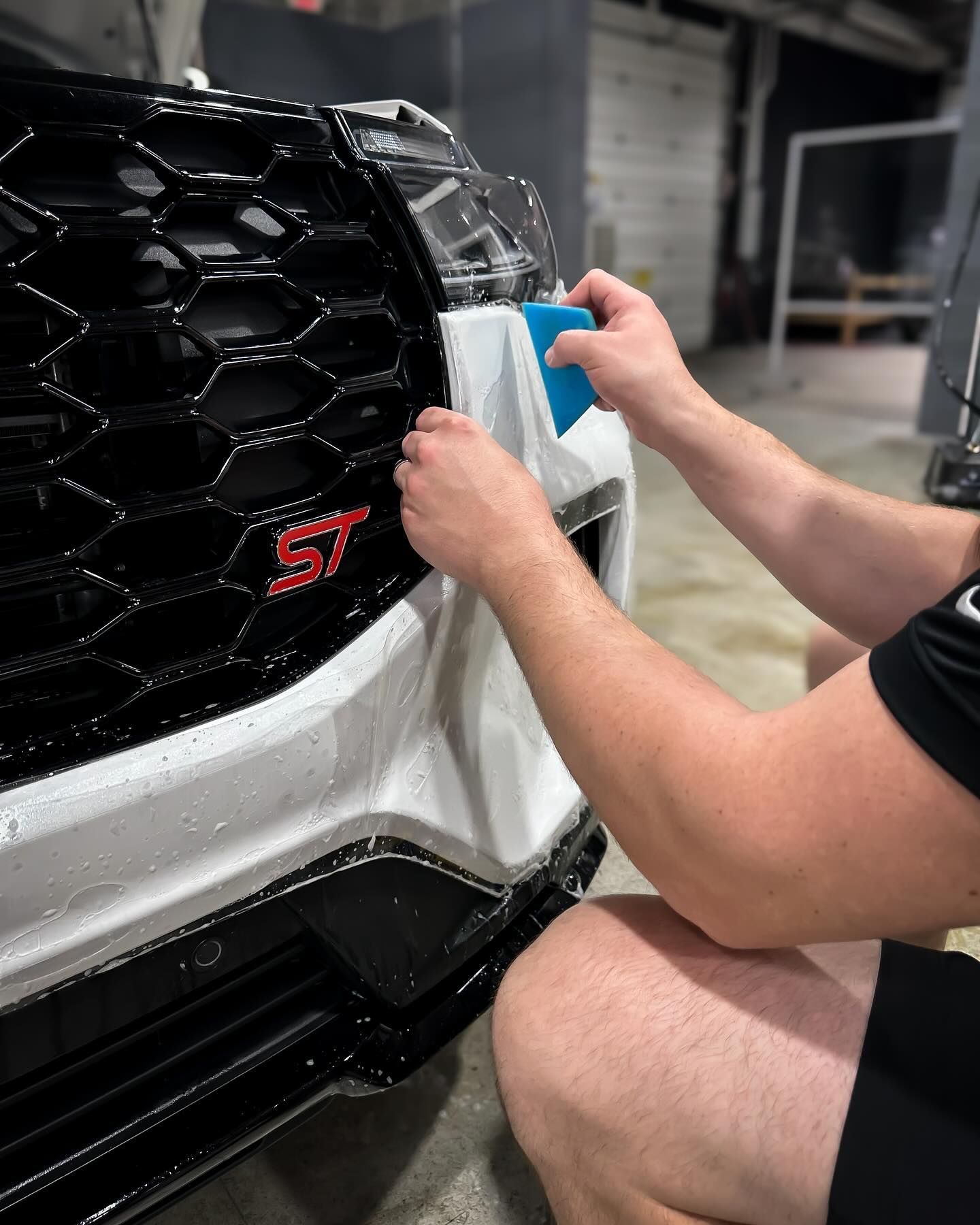 A man is cleaning the front of a white car with a towel.