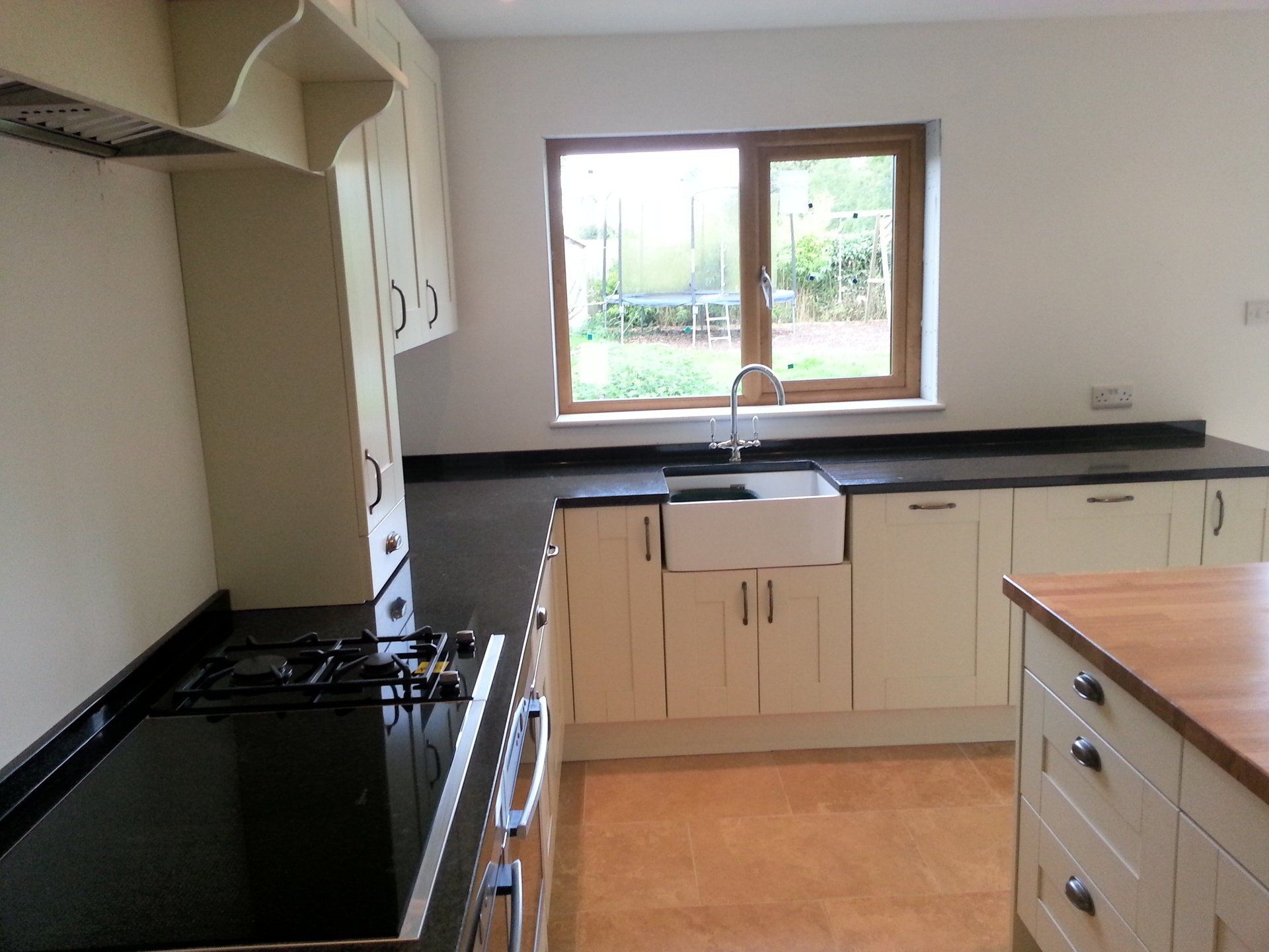 Cream-colored kitchen cabinets with dark countertops. A gas range, window over a farmhouse sink, and wooden floor.
