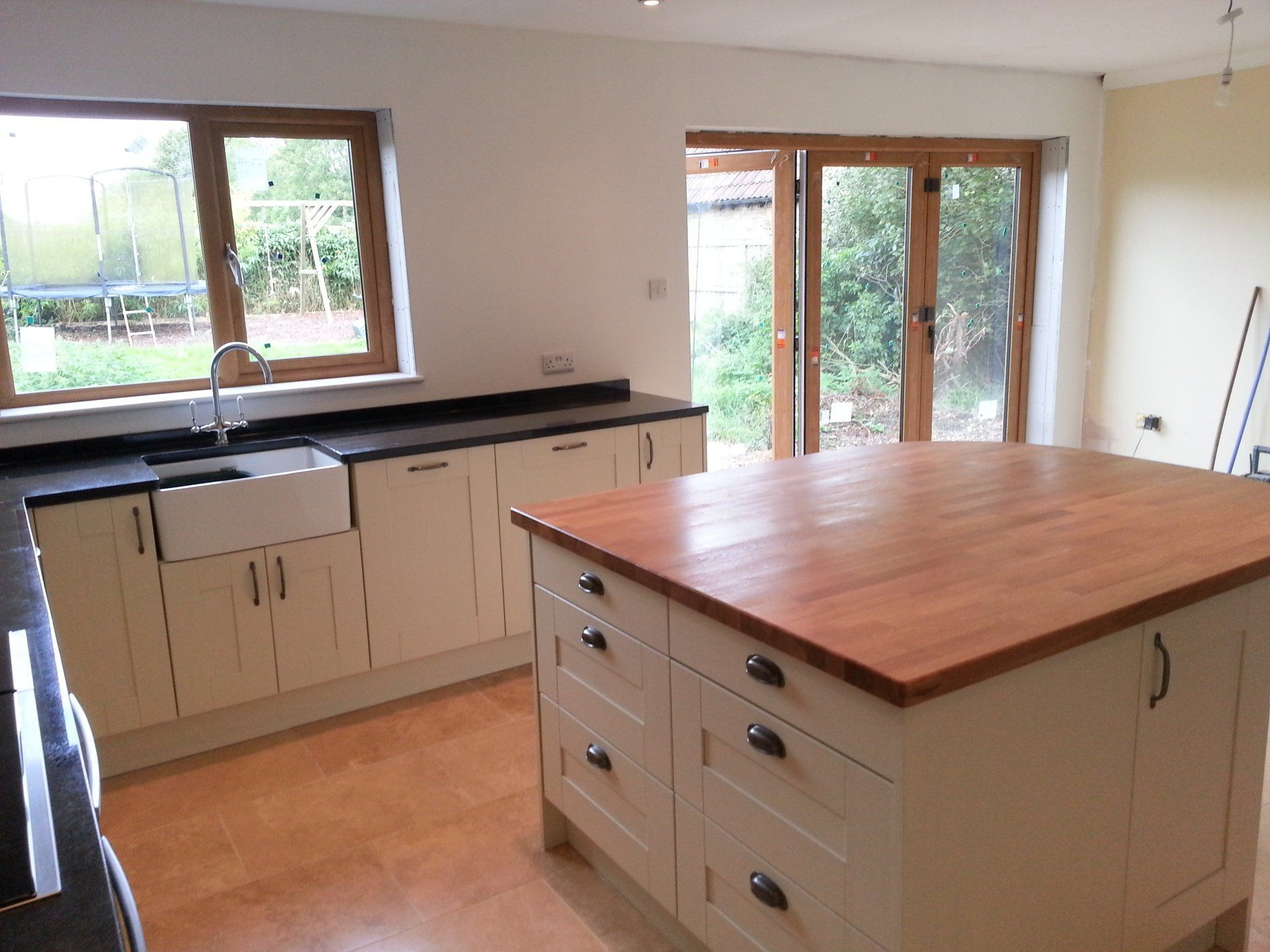 Cream kitchen with butcher block island, cabinetry, and windows overlooking a garden.