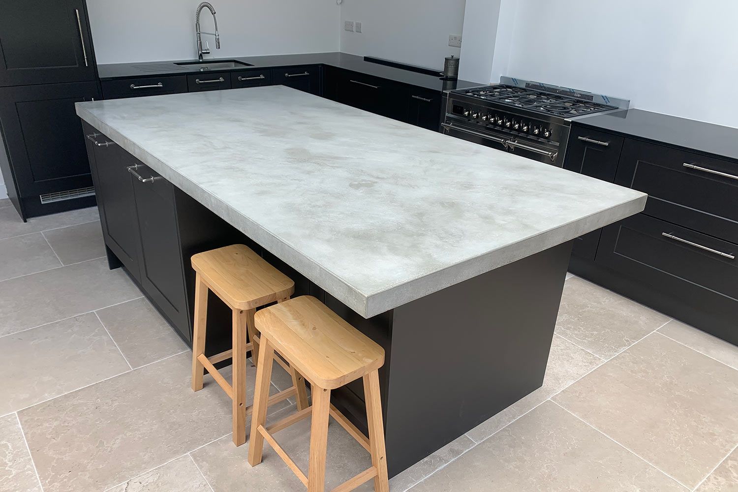 Kitchen island with gray countertop, black cabinets, and two wooden stools.