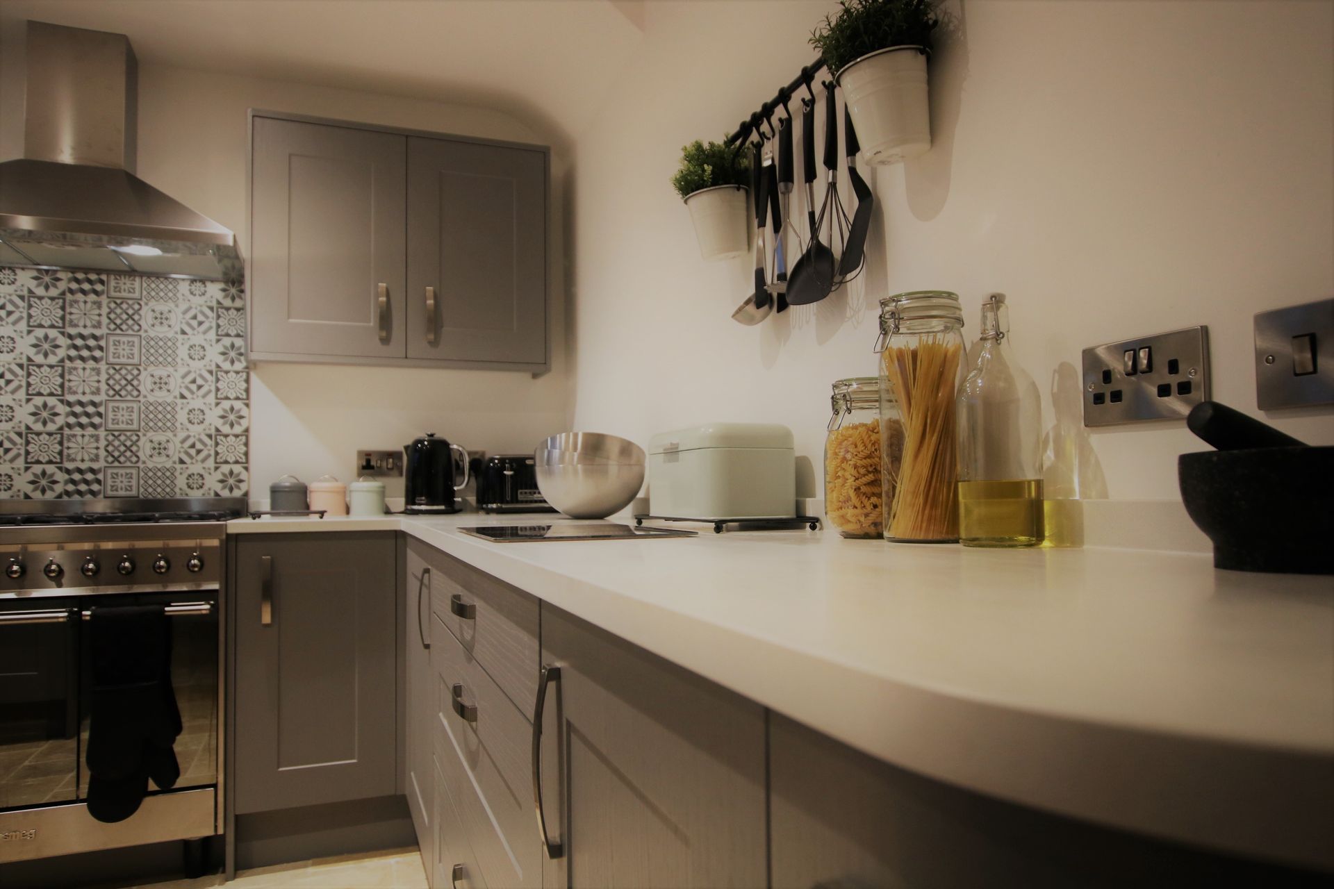 Grey kitchen with white countertops, stainless steel appliances, and jars of food.