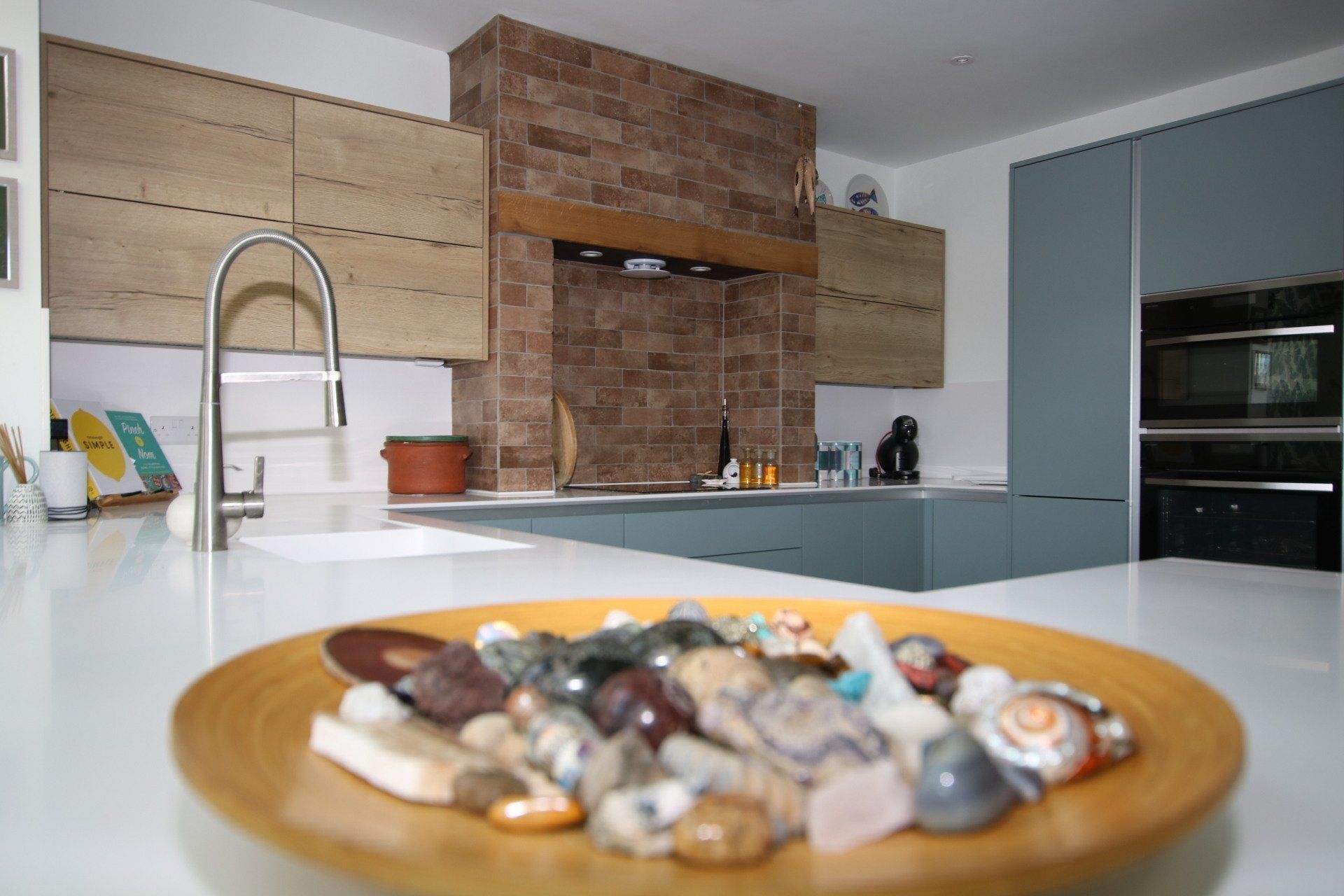 A kitchen with a wooden bowl of stones on a countertop, blue cabinets, and brick accent.
