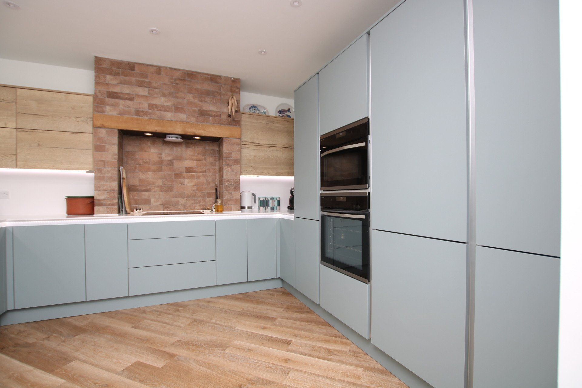 Modern kitchen with light blue cabinets, brick accent wall, and wood flooring.