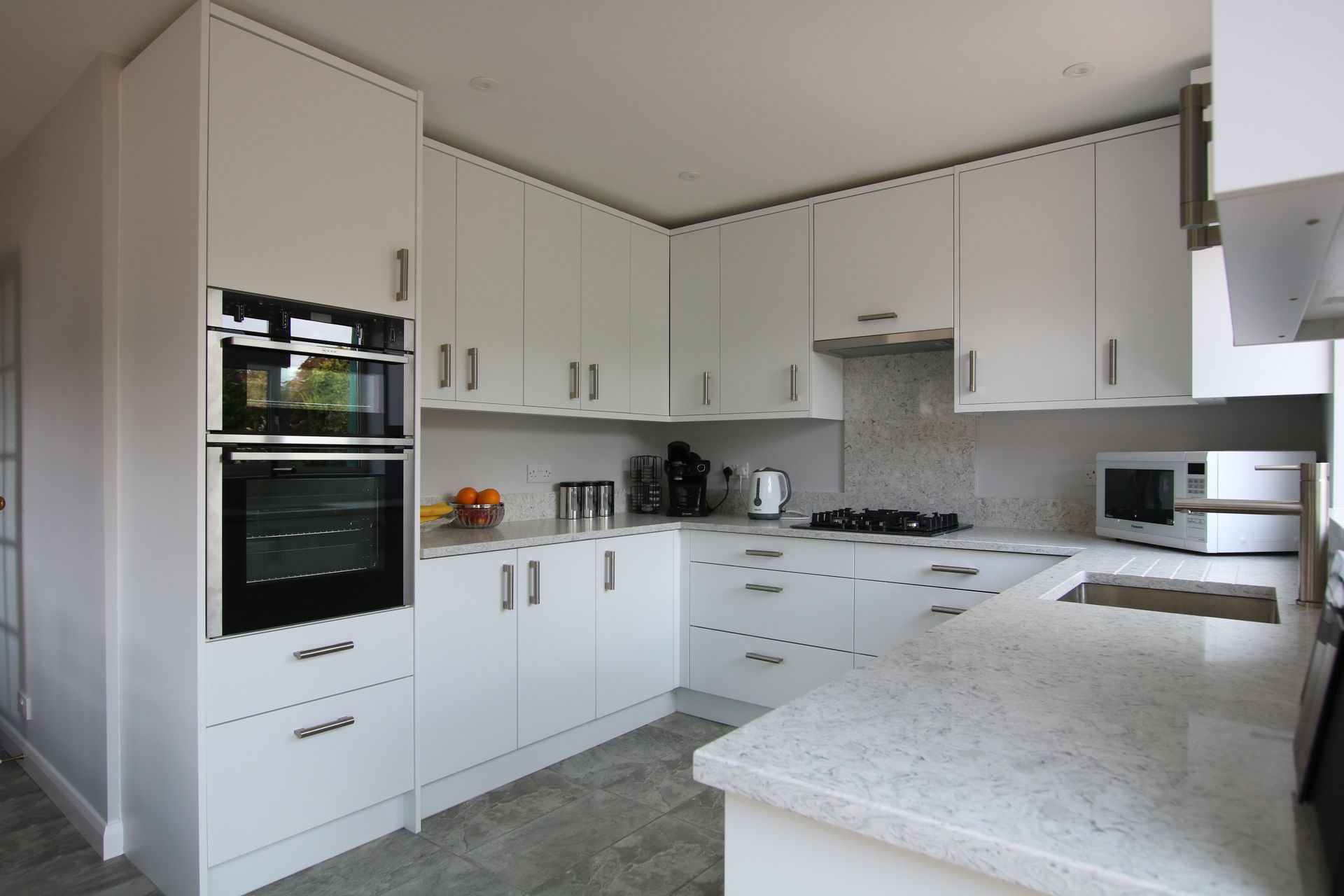 White kitchen with upper and lower cabinets, built-in oven, countertop, microwave, and stovetop.