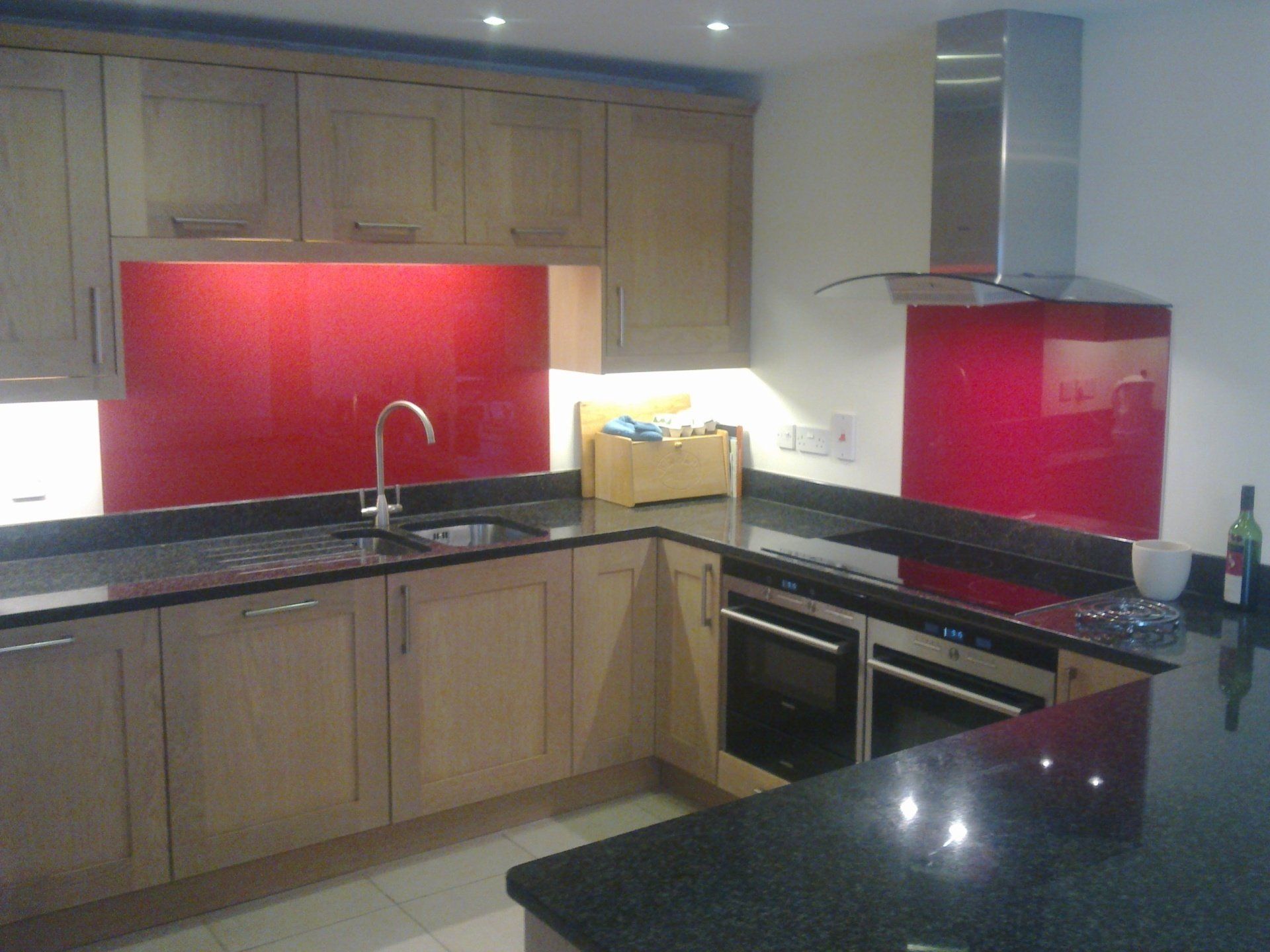 Kitchen with light wood cabinets, red backsplash, black countertops, and stainless steel appliances.