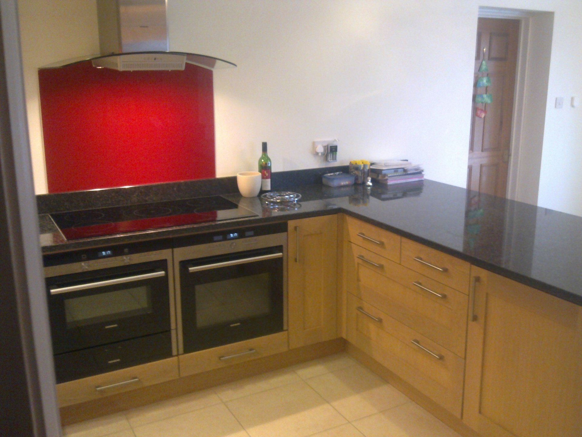 Modern kitchen with red backsplash, black countertops, wooden cabinets, and built-in ovens.