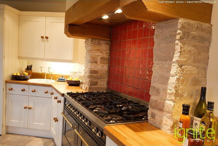 Kitchen with white cabinets, wooden countertops, and a stove with a red tile backsplash.