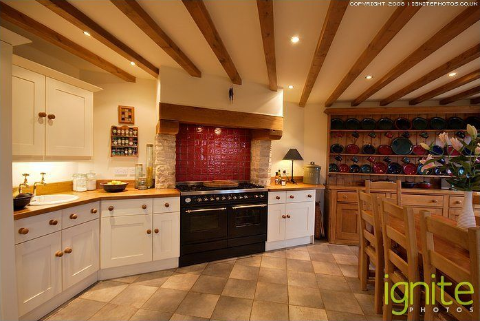 Kitchen with white cabinets, tile floor, red backsplash, and wood beams.