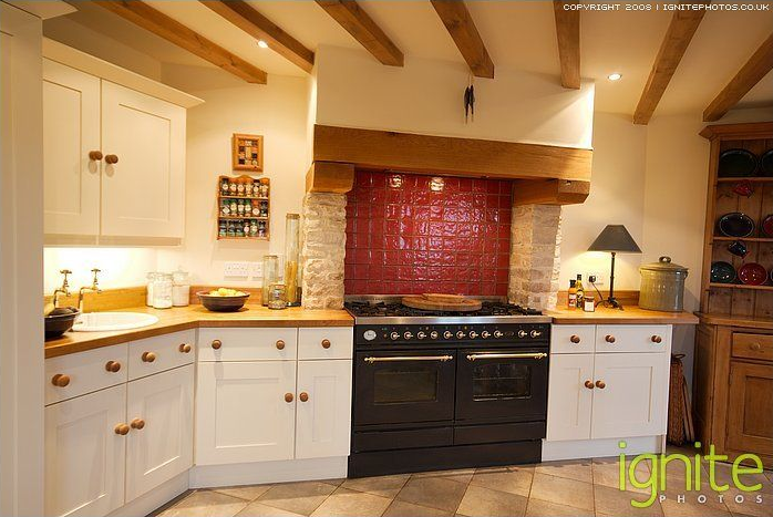 Cozy kitchen with white cabinets, wooden beams, a black stove, and a red tile backsplash.