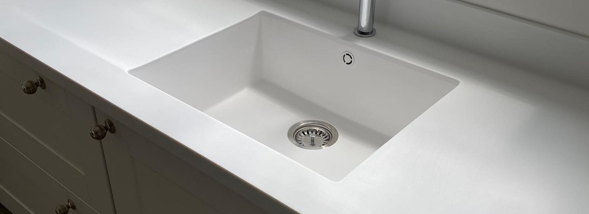 White kitchen sink built into a white countertop. Chrome drain cover and faucet.