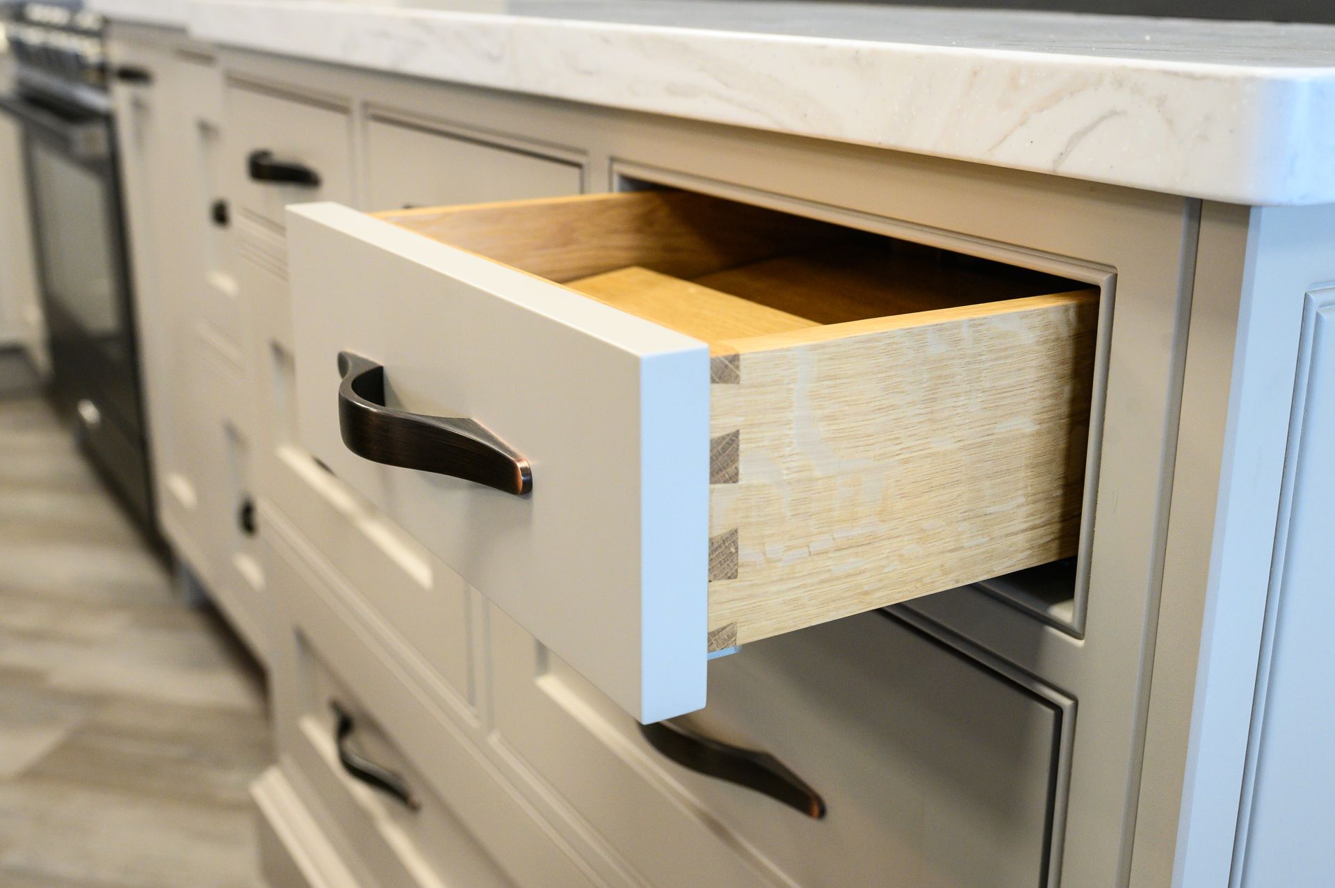 Open kitchen drawer with dovetail joints, gray paint, black handle, and wooden interior.