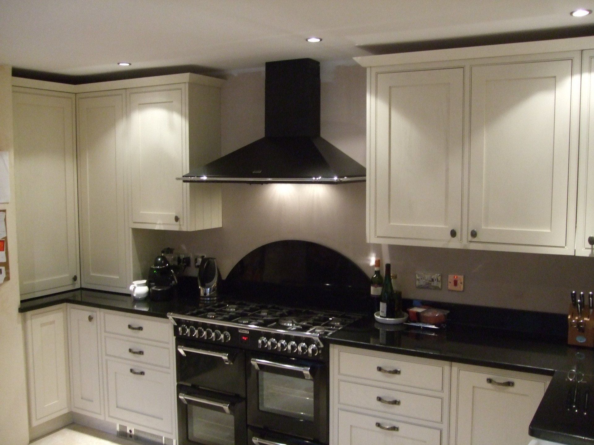 Cream-colored kitchen cabinets with black countertops and a black range hood above the oven.