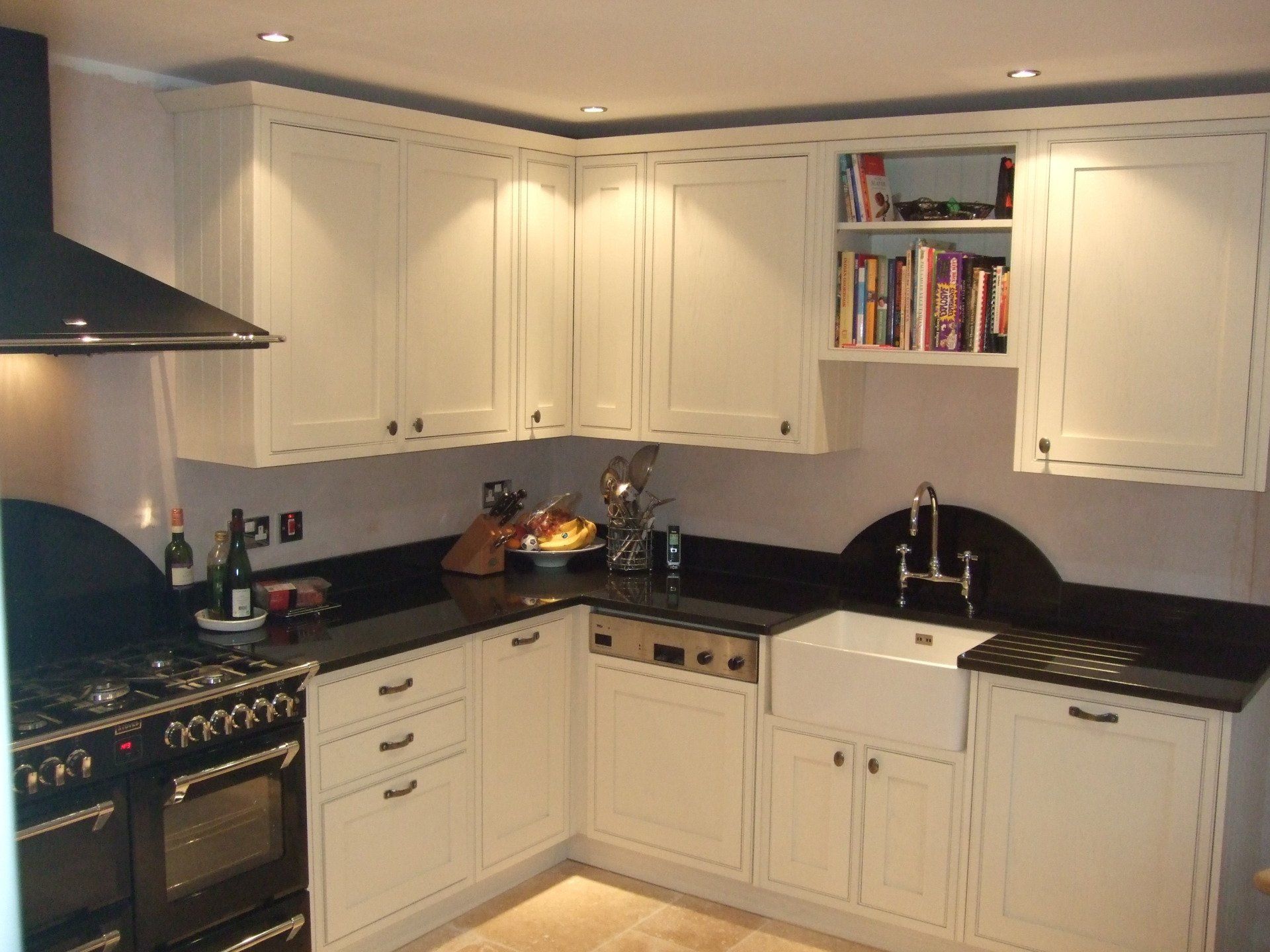 Cream-colored kitchen cabinets and black countertops. A farmhouse sink and stovetop are visible, with books on a shelf.
