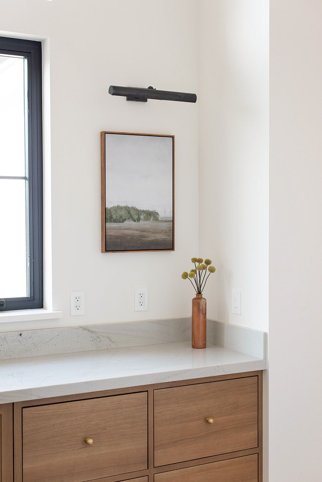 a bathroom vanity with a picture on the wall above it and a vase of flowers on the counter .