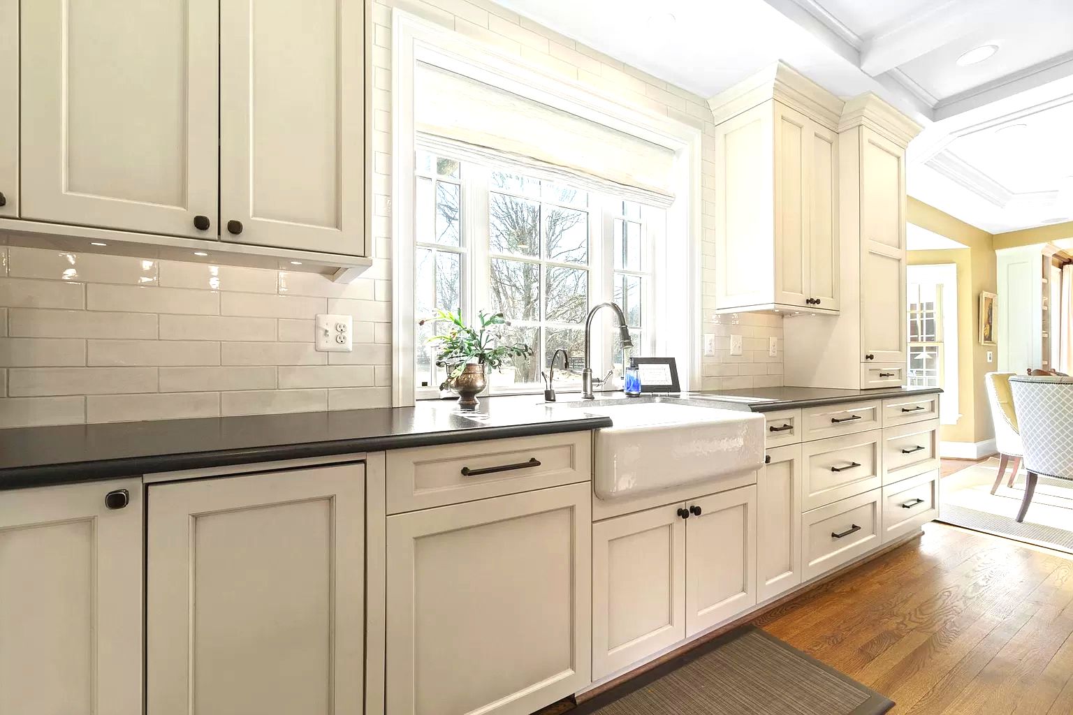 a kitchen with white cabinets , black counter tops , a sink and a window .