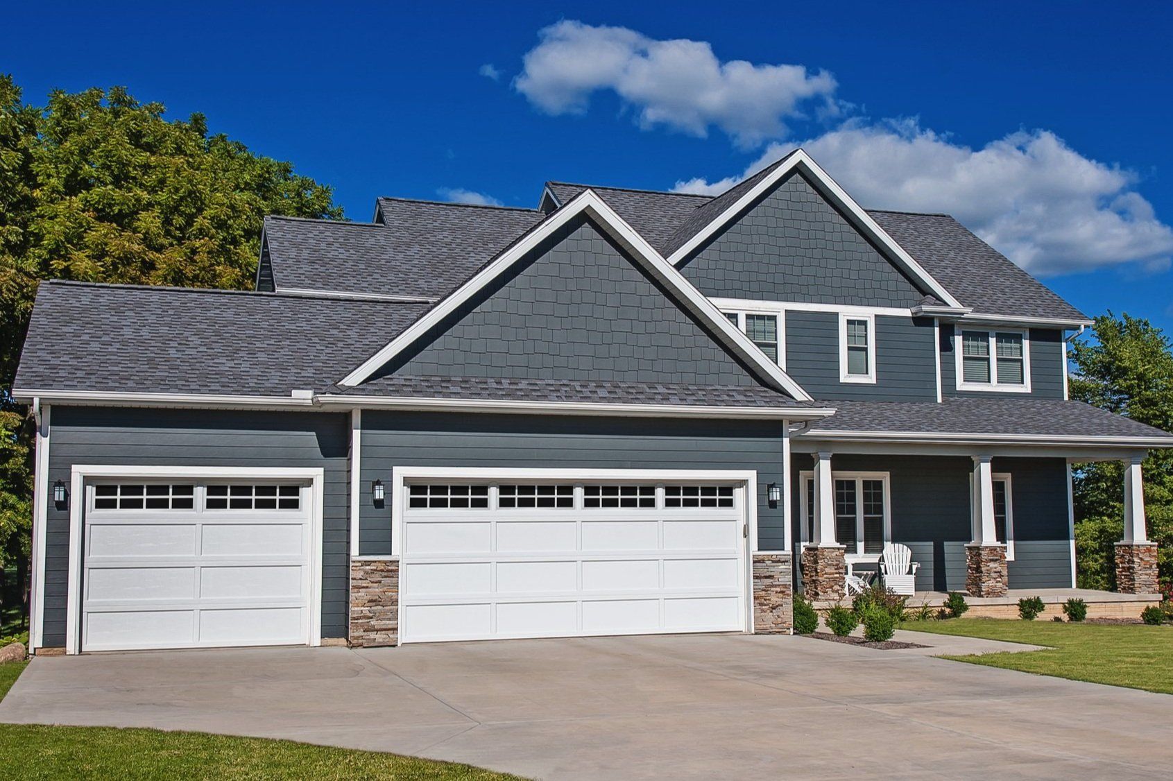 A large house with a gray siding and white garage doors