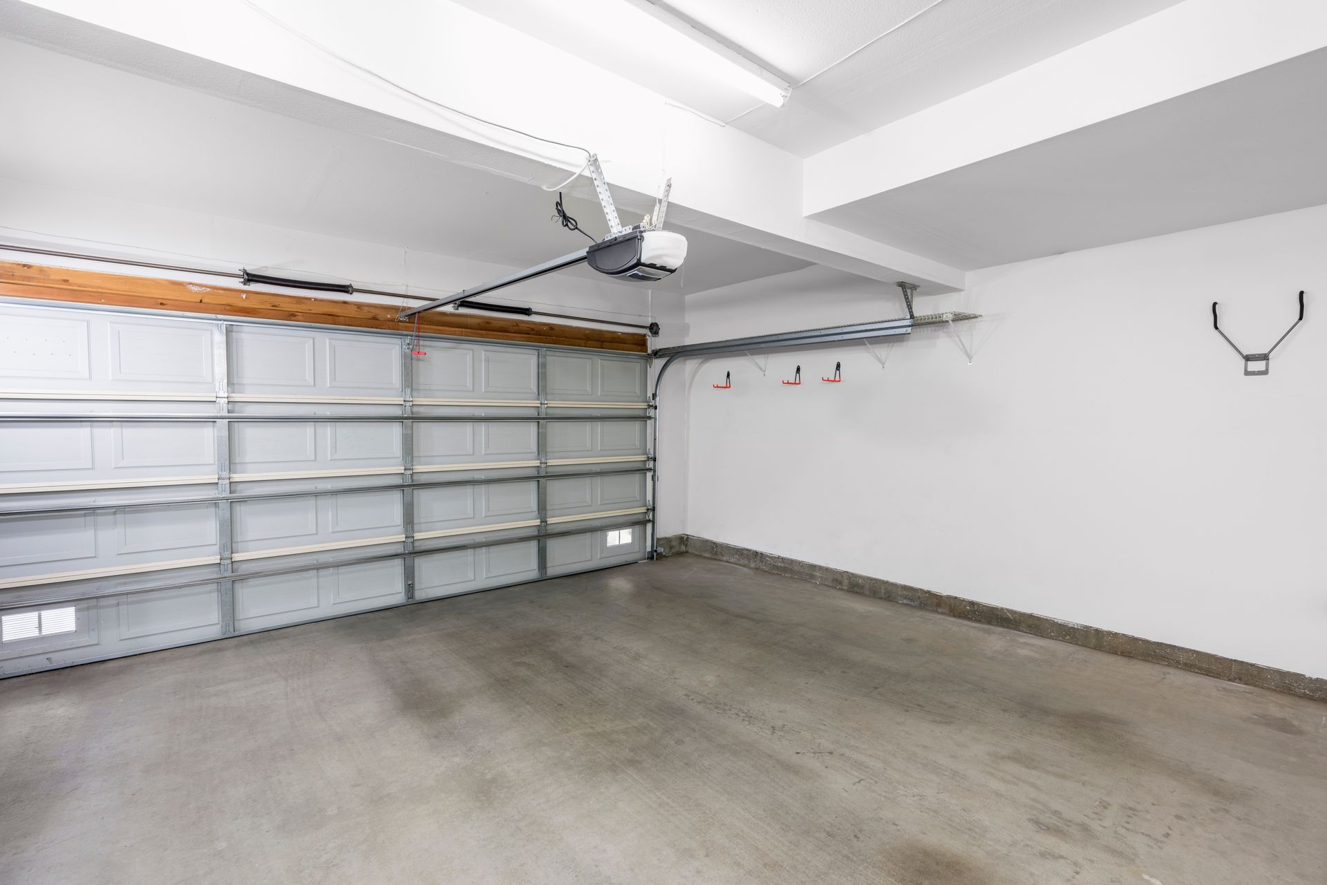 Empty garage with a gray concrete floor and white walls. Garage door is open.