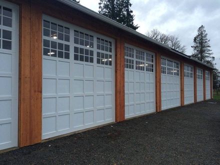 White garage doors with small windows on a wooden building. Gravel ground, overcast sky.