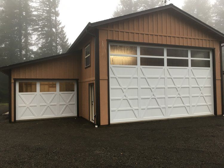 Two-story brown garage building with white garage doors and a small window. Gray gravel driveway. Foggy outdoor setting.