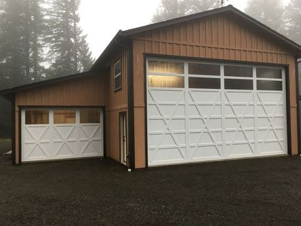 Two-story brown garage with two white garage doors, one larger than the other. The setting is foggy.